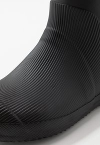 Svart gummistövlar med ribbad textur, en slät tå och en strukturerad sula med ett mönstrat grepp.