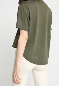 Polo shirt de malla ligera en color verde oliva, con mangas cortas, que presenta un corte ligeramente holgado y sutiles perforaciones por toda la prenda.