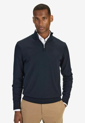Mörkblå kvart dragkedja sweatshirt i mjukt tyg, med ribbat fåll och ärmslut, kombinerad med en vit skjorta under.