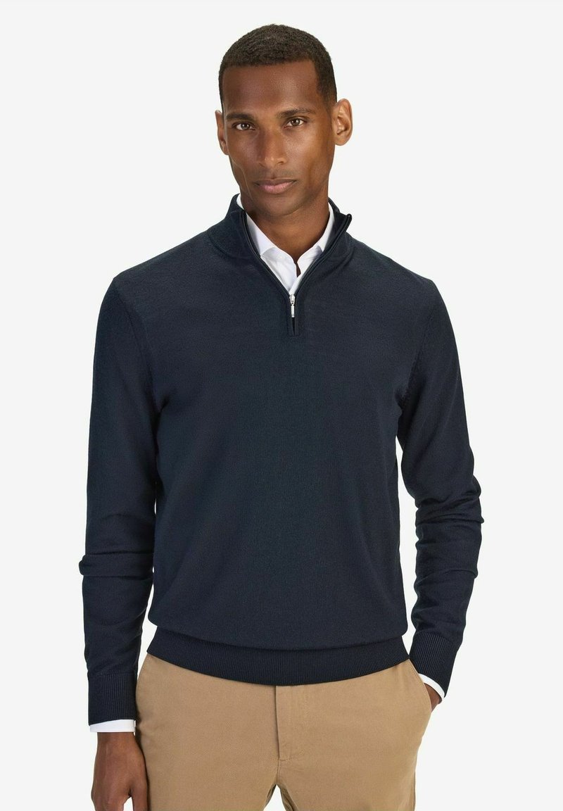 Mörkblå kvart dragkedja sweatshirt i mjukt tyg, med ribbat fåll och ärmslut, kombinerad med en vit skjorta under.