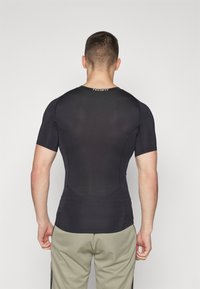 Sort kortærmet træningsskjorte med et tætsiddende design og struktureret stof, der har en rund hals og brandnavnet "TECHFIT" på ryggen.