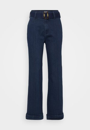 Donkerblauwe denim broek met een wijde pijpdesign, voorzien van een riem met een grote metalen gesp en zichtbare stiksels.