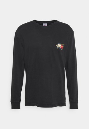 T-shirt noir à manches longues avec un petit graphique, shorts blancs, baskets noires avec une semelle à motifs, et un chapeau de seau blanc.
