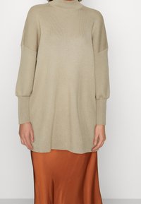 Pullover a coste beige con colletto alto e maniche oversize, abbinato a una gonna in satin arancione, con una texture liscia.