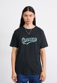 Črna bombažna majica s kratkimi rokavi in krožnim izrezom, na kateri je na prsih velik turkizno modri logotip "Converse".