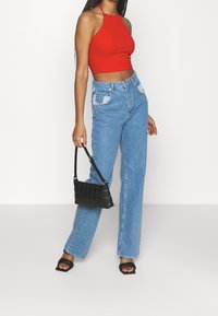Top corto rosso a righe, jeans blu chiaro a vita alta con tasche applicate, borsa a tracolla nera trapuntata e sandali neri con tacco e punta squadrata.