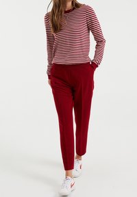 Röd randig tröja med långa ärmar, matchad med röda tapered byxor. Skorna är vita med röda detaljer. Enkel, avslappnad outfitdesign.