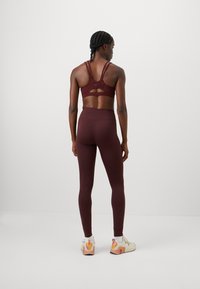 Bordeaux sports-bh med mesh-detaljer og racerback-design, kombinert med matchende høyt midje tights og lyse treningssko.