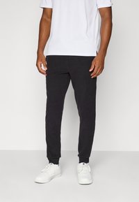Zwarte joggingsbroek van een zachte stof met elastische boorden, gecombineerd met een eenvoudig wit T-shirt met korte mouwen en witte sneakers.