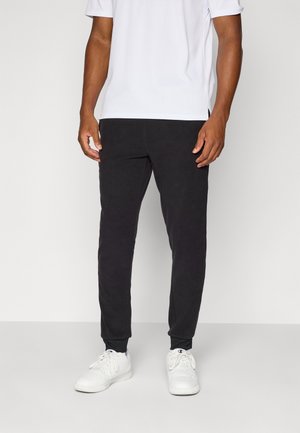 Black jogger pants in a soft fabric with elastic cuffs, paired with a plain white short-sleeve shirt and white sneakers.