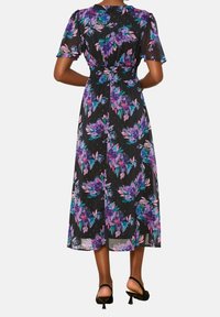 Maxikjol i lätt, transparent tyg med svart bakgrund och färgglada blommönster i lila och rosa. Korta ärmar och elastiskt midjeband.