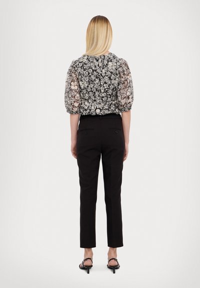 Musta housut, joissa on slim fit -leikkaus ja napit, yhdistettynä läpikuultavaan kukkakuosiset paitaan, jossa on puffihihat.