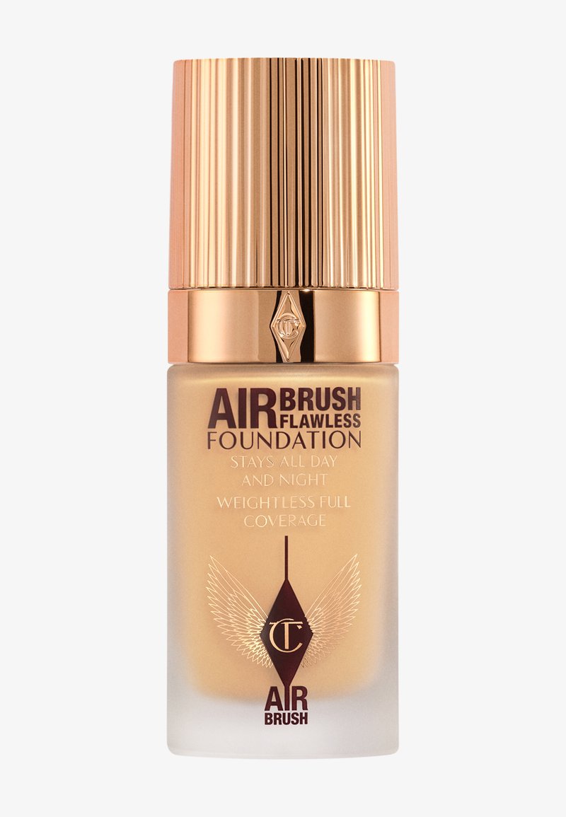 Fond de teint Airbrush Flawless dans un flacon en verre transparent avec un capuchon doré texturé. Présente un texte en gras et des accents en relief en forme d'aile.