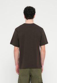 Καφέ βαμβακερό T-shirt με κοντά μανίκια, στρογγυλή λαιμόκοψη και άνετη εφαρμογή. Ομαλή υφή. Η πίσω όψη δεν παρουσιάζει ορατά σχέδια ή διακοσμητικά στοιχεία.