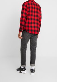 Punainen ja musta ruudullinen pitkähiha-paita, yhdistetty tummanharmaisiin farkkuihin. Tennarit ovat mustavalkoiset kangaselementeillä.