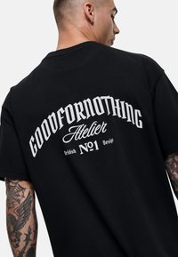 Zwart katoenen T-shirt met een grote witte grafische tekstontwerp op de achterkant, met merk elementen en een ronde hals stijl.