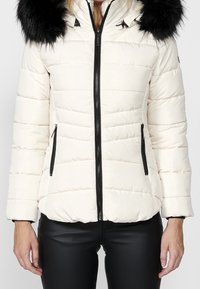 Giacca puffa di un crema chiaro con zip e tasche nere, dotata di cappuccio in pelliccia nera removibile e texture trapuntata.