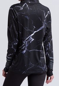 Maglia sportiva nera a maniche lunghe con motivo marmorizzato bianco e aperture per il pollice, indossata da una persona vista di spalle.