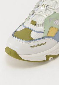 Tênis branco com realces multicoloridos em verde, azul e bege. Apresenta um cabedal em malha, sola resistente e o logotipo "KARL LAGERFELD" na lateral.