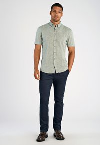 Korte mouwen button-up shirt in lichtgroene textuurstof, gecombineerd met donkerblauwe slim-fit broek en bruine nette schoenen.