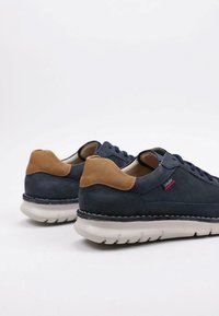 Zapatillas de gamuza azul marino con un talón de cuero marrón claro, suela de goma blanca y detalles de costura azul. Diseño clásico de cordones.