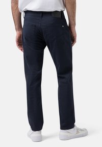 Navyblaue Baumwollhose mit geradem Bein, ausgestattet mit zwei Gesäßtaschen und dezenten Steppdetails, kombiniert mit weißen Sneakers.
