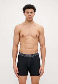 Boxerii negri, cu un design ajustat, dintr-un material elastic, și o talie lată cu logo-ul "UNDER ARMOUR" în gri.