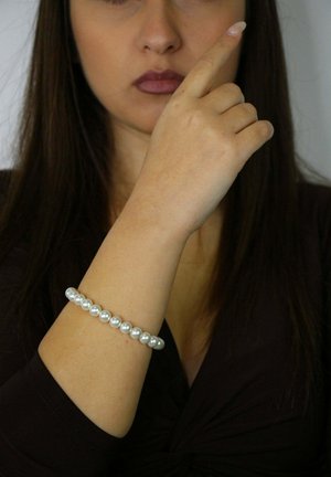 Weißes Perlenarmband mit glatter, glänzender Oberfläche, bestehend aus gleichmäßig großen Perlen, die auf einem flexiblen Band aufgefädelt sind und am Handgelenk getragen werden.