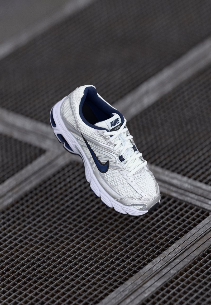 Biały i granatowy but do biegania marki Nike, z teksturowaną cholewką z siateczki, wyściełaną podeszwą i charakterystycznym logo po boku.
