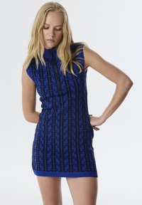 Gebreide mini-jurk met een blauw en zwart geometrisch patroon, hoge halslijn en mouwloos ontwerp, met een ritssluiting aan de voorkant.