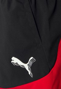 Mustat ja punaiset urheilushortsit, joissa on näkyvä valkoinen Puman logo. Valmistettu kevyestä ja sileäpintaisesta kankaasta. Korostetut taskut.