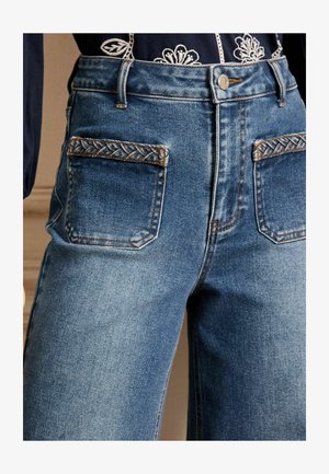Aukšto juosmens mėlyni džinsai su pintomis detalėmis gale ant kišenių, turintys klasikinį penkių kišenių dizainą ir šiek tiek siaurėjantys blauzdas.