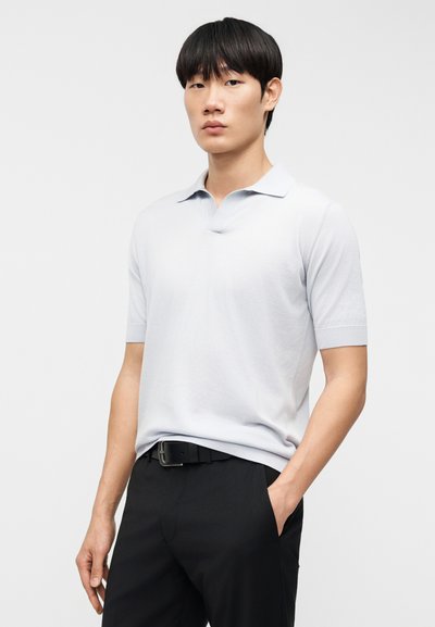 Világos szürke rövid ujjú galléros póló puha anyagból és lapos gallérral. Fekete nadrággal és övvel viselve. Minimalista dizájn, minták nélkül.