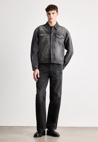 Jachetă din denim negru cu un finisaj ușor decolorat, dotată cu două buzunare frontale, asortată cu blugi negri cu croială dreaptă și încălțăminte din piele neagră.