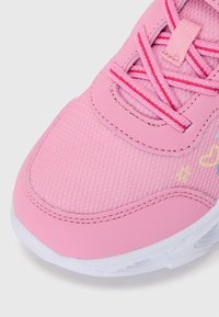 Close-up de um ténis cor-de-rosa com tecido texturizado, atacadores e desenhos decorativos de estrela amarela e coração numa sola branca.