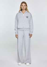 Grijze ritssluiting hoodie met een trekkoord capuchon, gecombineerd met bijpassende wijde sweatpants. Bevat een logo-print op de borst en boven de bovenbeen.