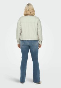 Chaqueta corta de color gris claro con una textura suave y hombros caídos. Combinada con jeans de campana azules, que cuentan con bolsillos traseros y un diseño sencillo.