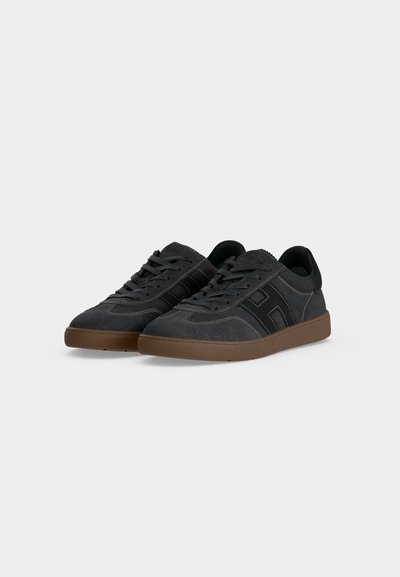 Paire de baskets en daim gris foncé avec des accents noirs et des semelles en caoutchouc marron, présentée légèrement en angle sur fond blanc.