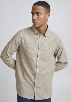 Camisa de botones a rayas en beige y marrón claro, con un bolsillo en el pecho, cuello y mangas largas de corte relajado. La textura parece suave.