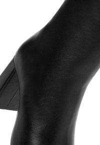 Zapato de tacón alto de cuero negro con un diseño elegante y curvado. Textura suave y tacón anguloso, sin patrones ni embellishments visibles.
