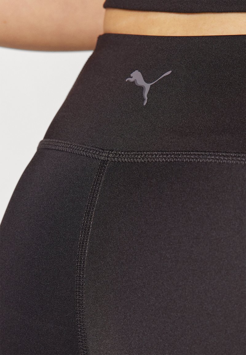 Leggings deportivos negros hechos de una tela elástica con una textura suave. Presenta un logo de Puma en color gris en la cintura y costuras planas.