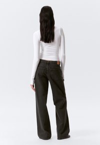 Jean large gris foncé avec taille haute, comportant deux poches arrière et une patch en cuir marron à la taille, associé à un haut blanc ajusté.