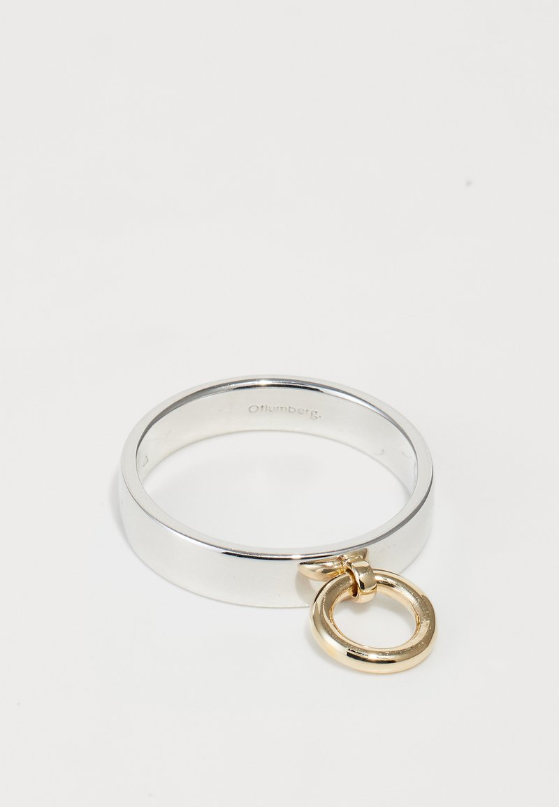 Srebrny pierścionek z gładką, szeroką obrączką oraz złotym okrągłym charmsiem przymocowanym do niego. Pierścionek ma błyszczące wykończenie i posiada wytłoczone logo wewnątrz.