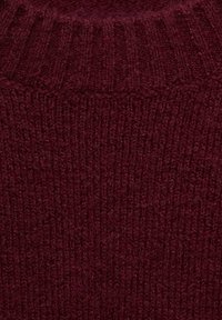 Burgundska pletena majica iz tkanine s rebrastim ovratnikom, ki ima teksturirano površino in dosleden šivni vzorec po celotni površini.