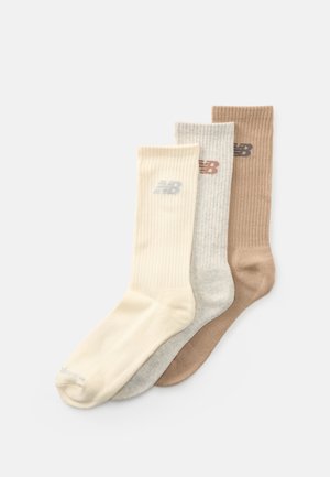 Trois paires de chaussettes de type crew côtelées en crème, gris clair et marron clair, avec un petit logo de marque près du haut.