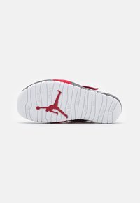 Vit yttersula med en röd Jordan-logotyp. Texturerade skåror för grepp. Inkluderar ord som "HOPPA", "SKIPPA" och "LEK" i upphöjd skrift.