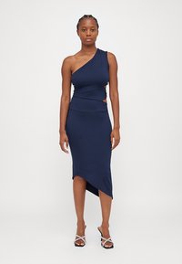 Robe asymétrique bleu marine à une épaule avec des découpes et une silhouette ajustée. Dotée d'une longueur mi-mollet et d'un ourlet asymétrique. Tissu lisse et extensible.
