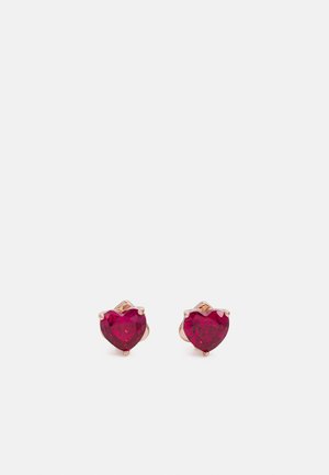 Brincos em forma de coração com uma pedra vermelho profundo montada em metal de tom rosé. Superfície lisa com quatro garras.
