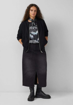 Zwarte bomberjack, graphic t-shirt met disco-print, zwarte denim rok met voorzijde split, en chunky zwarte laarzen. De textuur is glad en casual.