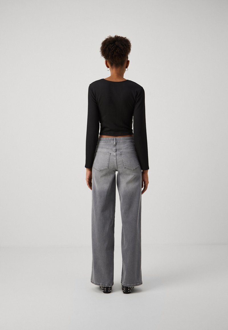 Haut noir à manches longues côtelé associé à un jean gris à jambes larges. Le jean possède des poches standards et une finition délavée avec des coutures visibles.